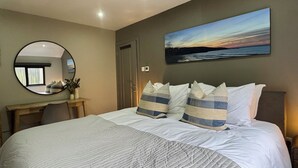 A bedroom with a large bed, a round mirror, a desk, and a painting on the wall. - Uno Moor Side (Carbis Bay)
