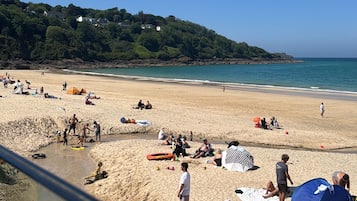 Una playa con gente tomando el sol, tiendas de campaña y un cielo despejado.