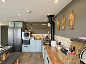 Eine moderne Küche mit einem Edelstahl-Kühlschrank, einem Backofen, einem Toaster und einem schwarzen Herd. Auf der Arbeitsplatte liegen Holz-Schneidebretter und ein Korb mit Küchenutensilien.