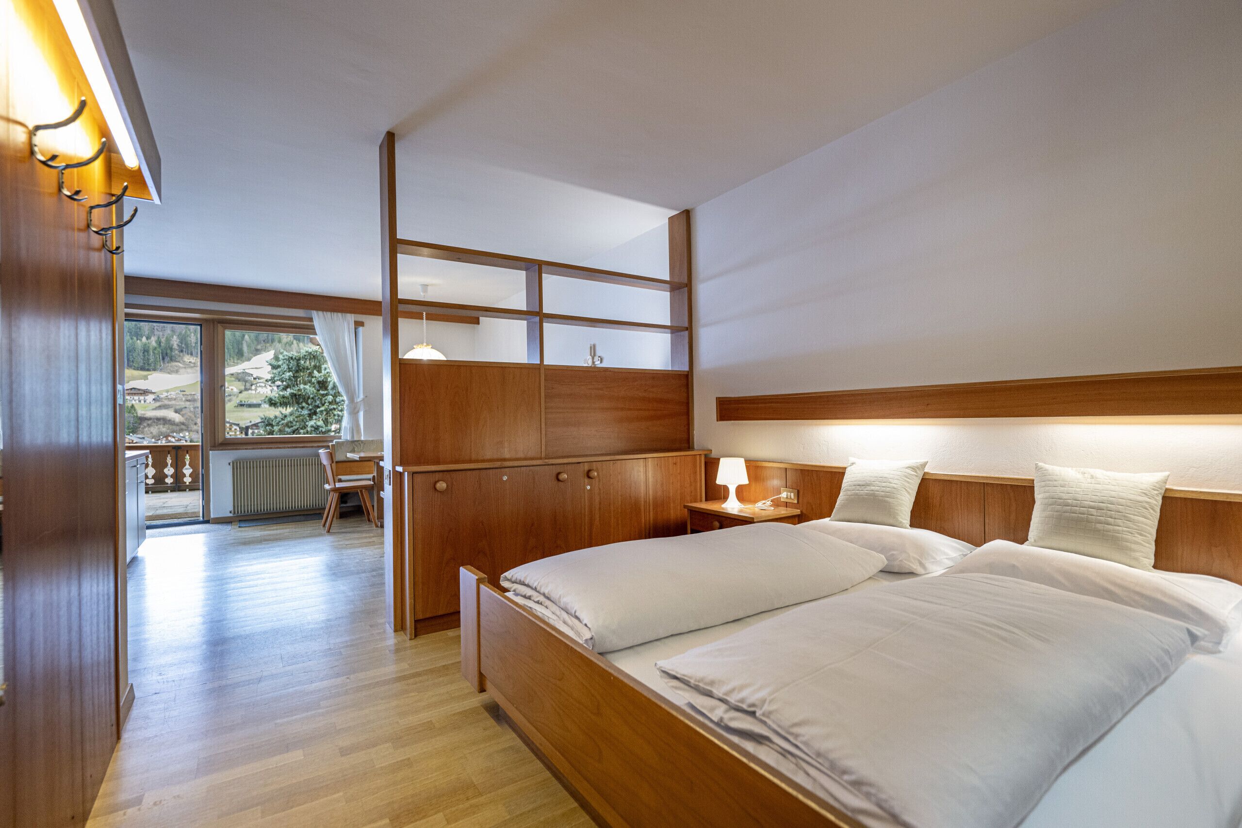 Una camera da letto con un letto di legno, un comodino con una lampada, un'armadio in legno e vista all'esterno da una grande finestra.