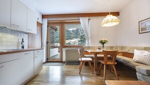 Une cuisine moderne avec un coin repas, un plancher en bois et une vue sur un paysage montagneux, visible à travers une grande fenêtre.