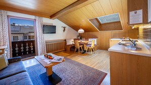 Une pièce chaleureuse et bien éclairée, avec un plafond en bois, un coin repas comprenant une table et des chaises, un coin cuisine avec un évier et un plan de travail, et une vue sur une montagne enneigée par la fenêtre.