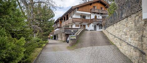 A traditional wooden building with balconies, a stone wall, and a paved pathway.