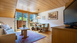 Un salón acogedor con techo de madera, un sofá, una mesa de comedor con sillas, un televisor y un ventanal con vistas al exterior.
