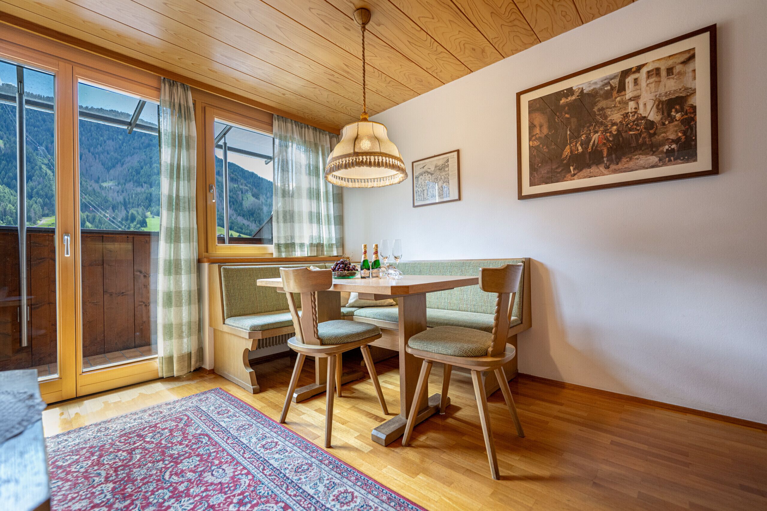 A dining area with a wooden table, two chairs, a bench, and a hanging light fixture.