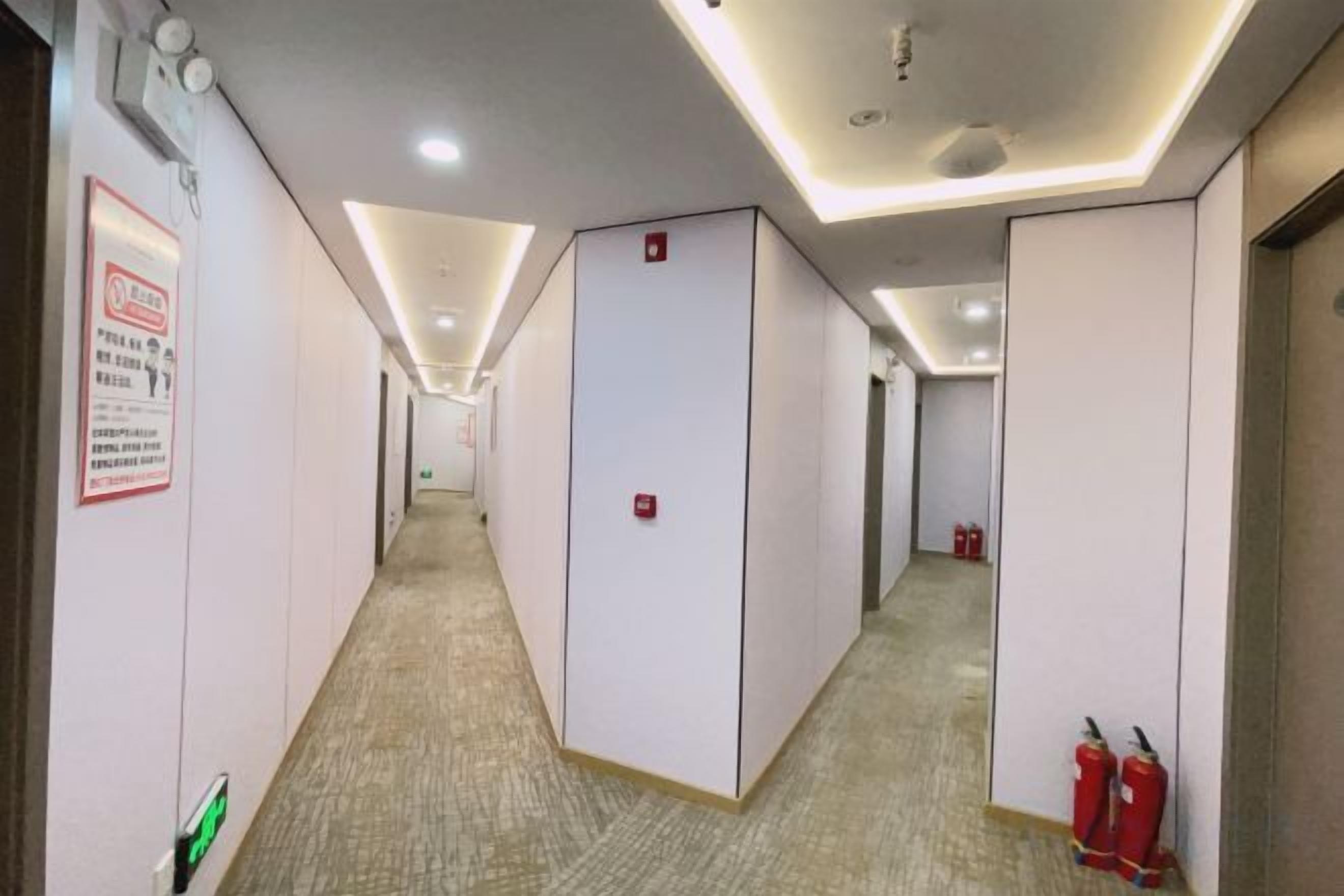 A corridor with white walls, a carpeted floor, and a ceiling with recessed lighting.