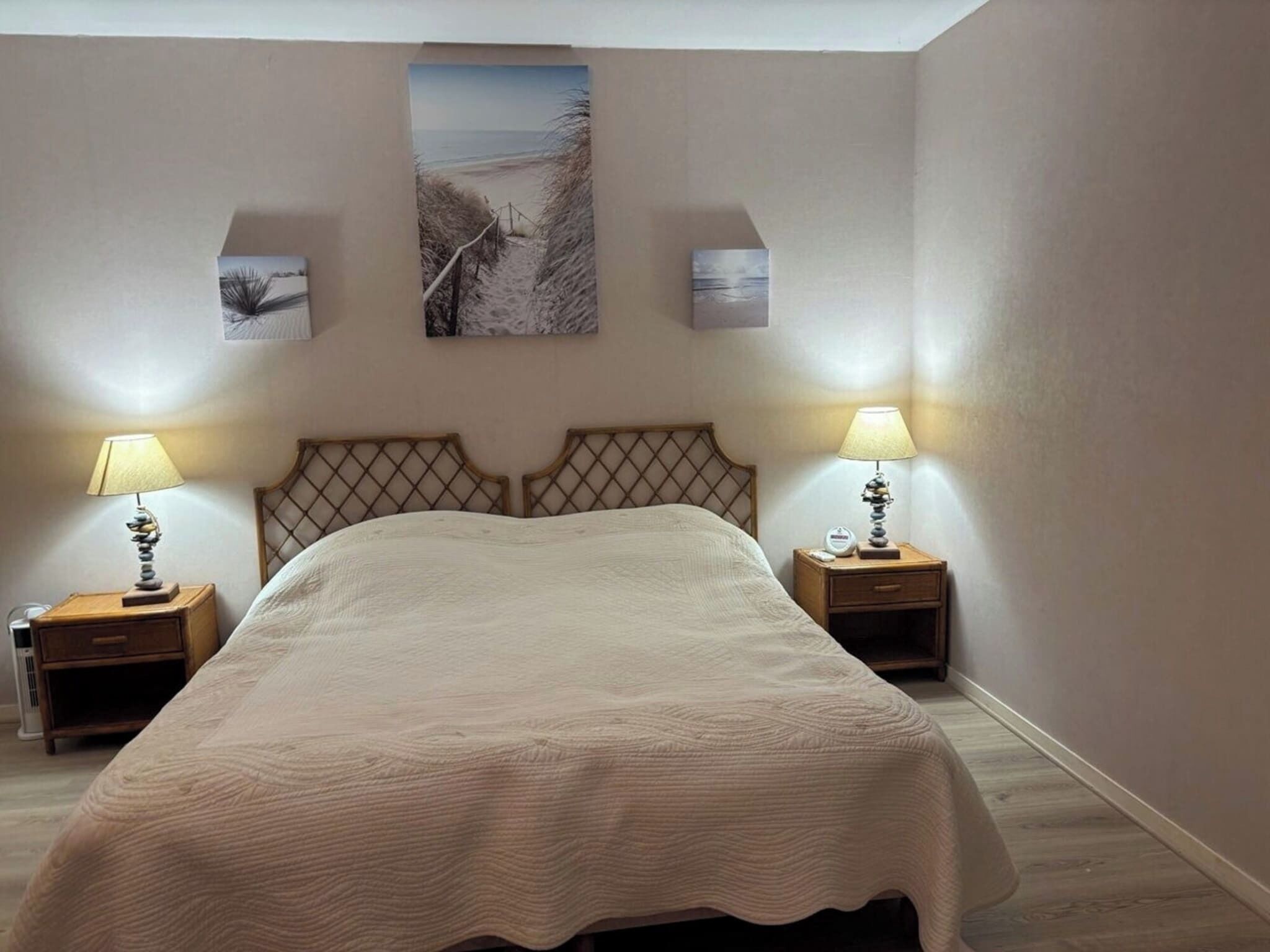 Une chambre à coucher avec un grand lit, deux tables de chevet avec des lampes et un tableau accroché au mur au-dessus du lit.