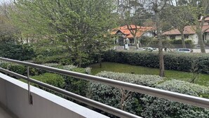 A balcony with a metal railing overlooking a residential area with houses, trees, and a well-maintained lawn. - Louisiana apartment (Arcachon)