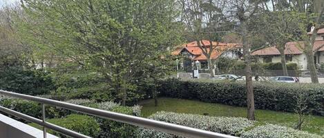 A balcony with a metal railing overlooking a residential area with houses, trees, and a well-maintained lawn.