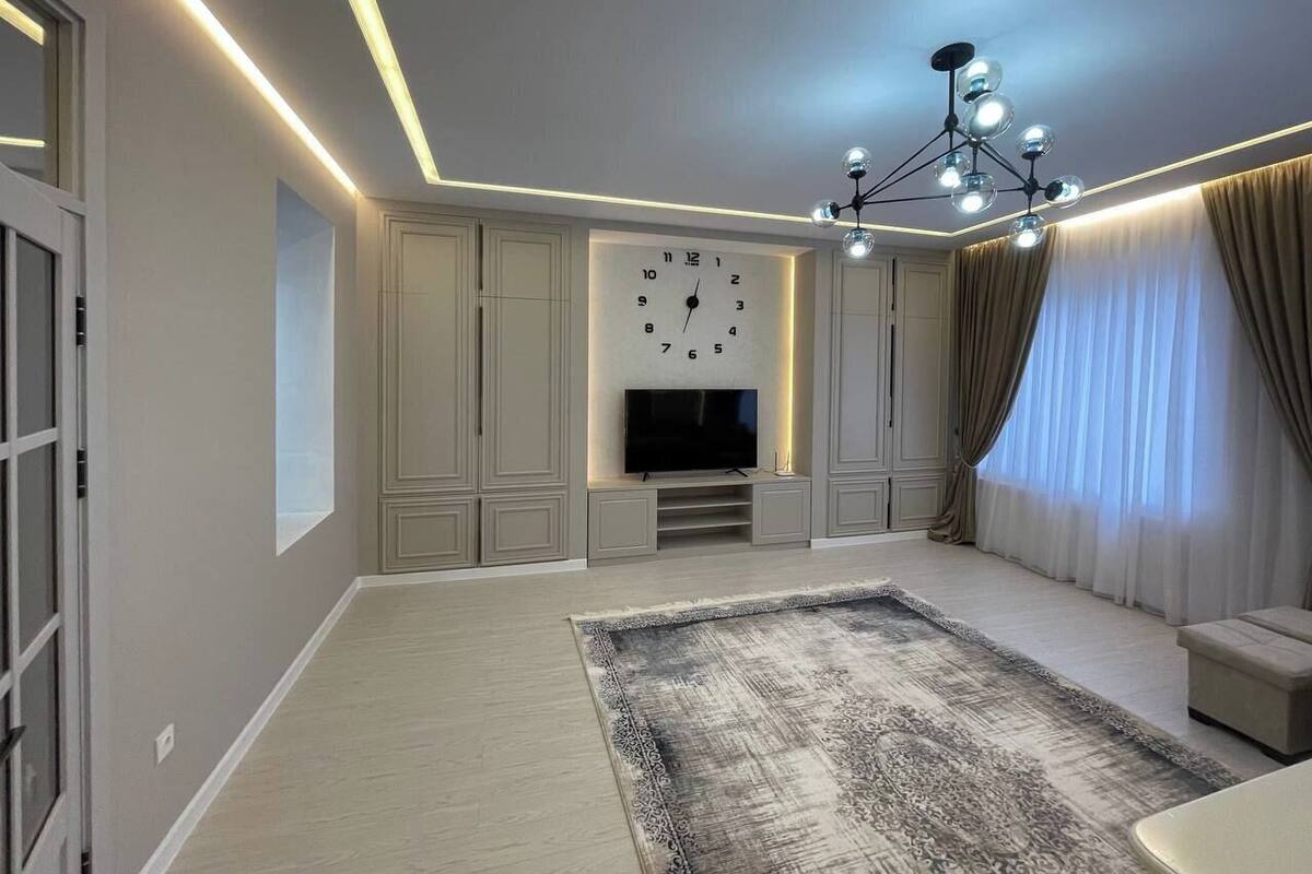 A modern living room with a flat-screen TV, a large rug, and a chandelier.