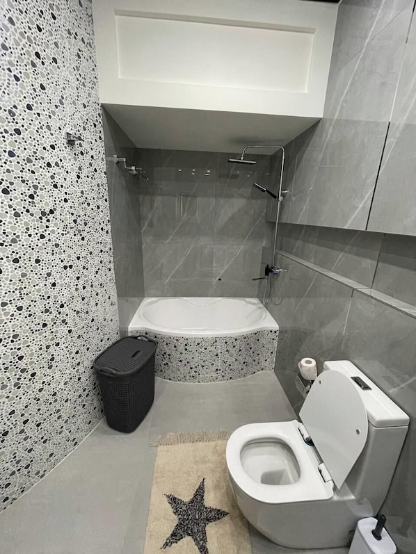 A modern bathroom with a bathtub, toilet, and a star-patterned rug. - Samarqand Same Hotel (Samarkand)
