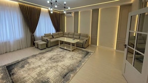 A modern living room with a sectional sofa, a coffee table, and a patterned rug. - Samarqand Same Hotel (Samarkand)