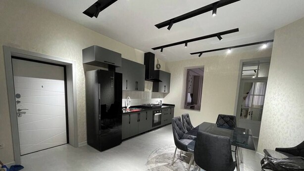 A modern kitchen with dark cabinetry, a dining area with a glass table, and a large grey rug. - Samarqand Same Hotel (Samarkand)