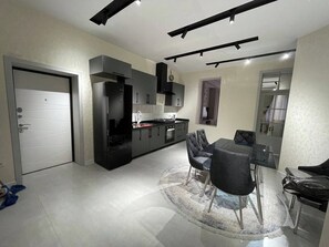 A modern kitchen with dark cabinetry, a dining area with a glass table, and a large grey rug. - Samarqand Same Hotel (Samarkand)