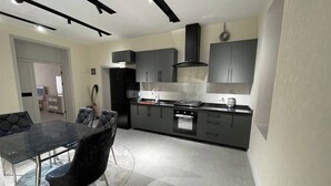A modern kitchen with dark cabinetry, a glass dining table, and a built-in oven. - Samarqand Same Hotel (Samarkand)
