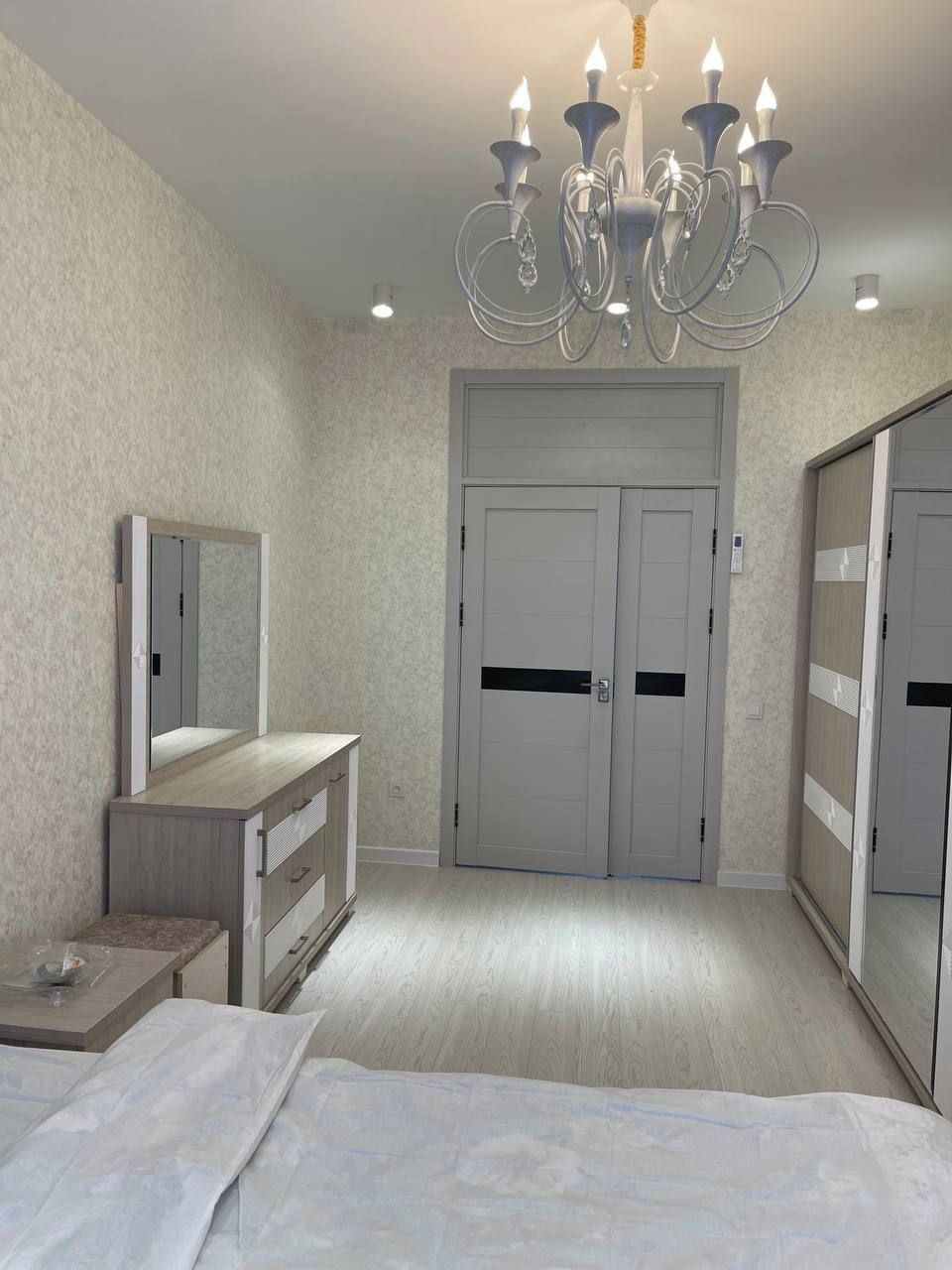 Een slaapkamer met een bed, een dressoir, een spiegel, een kroonluchter en een kledingkast.