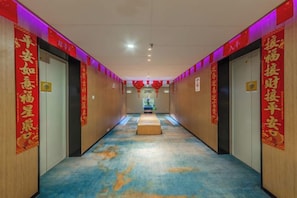 A hotel corridor with wooden walls, red banners, and a blue carpet.