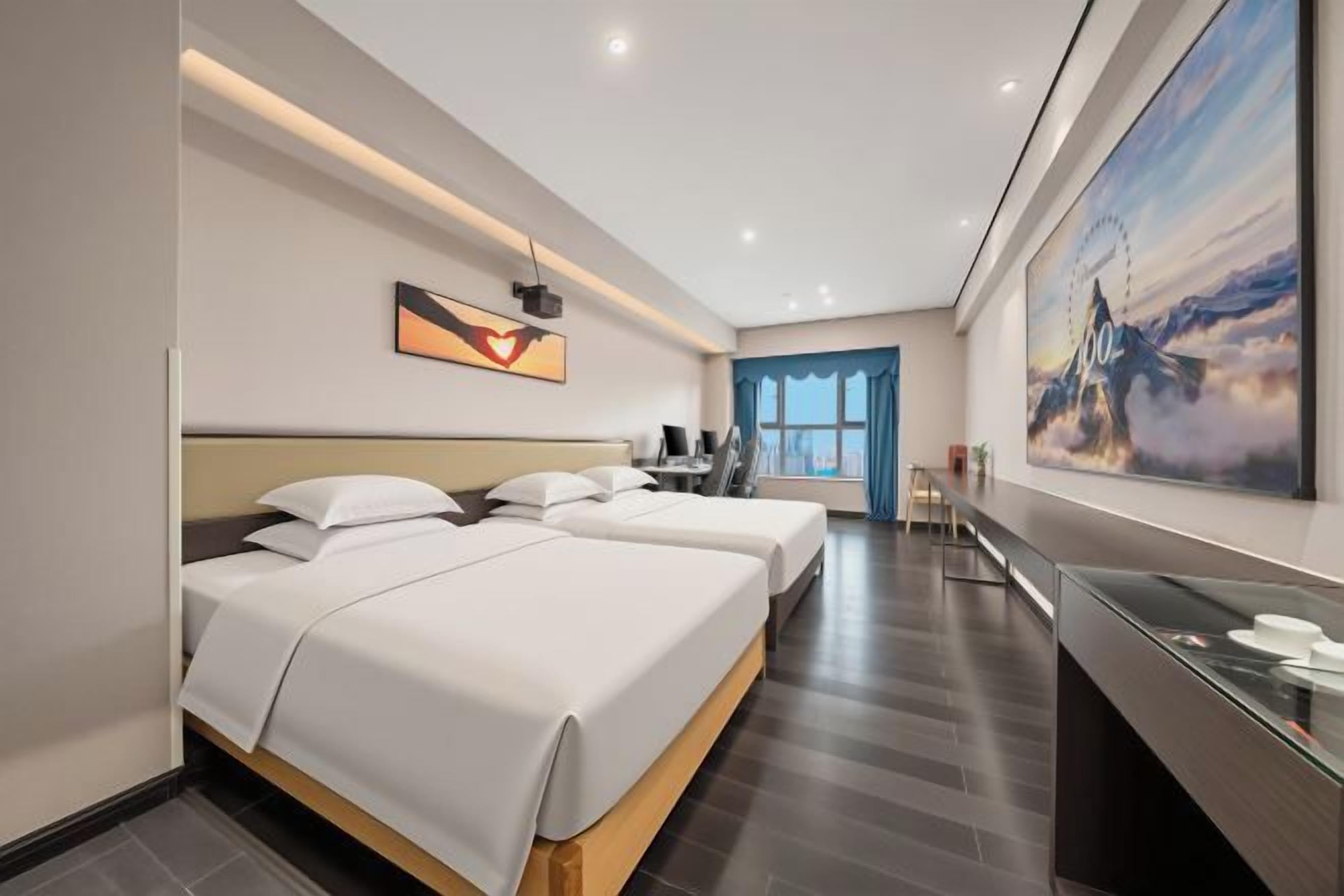 Une chambre d’hôtel avec deux lits, un bureau, une grande fenêtre et un tableau représentant un paysage de montagne.
