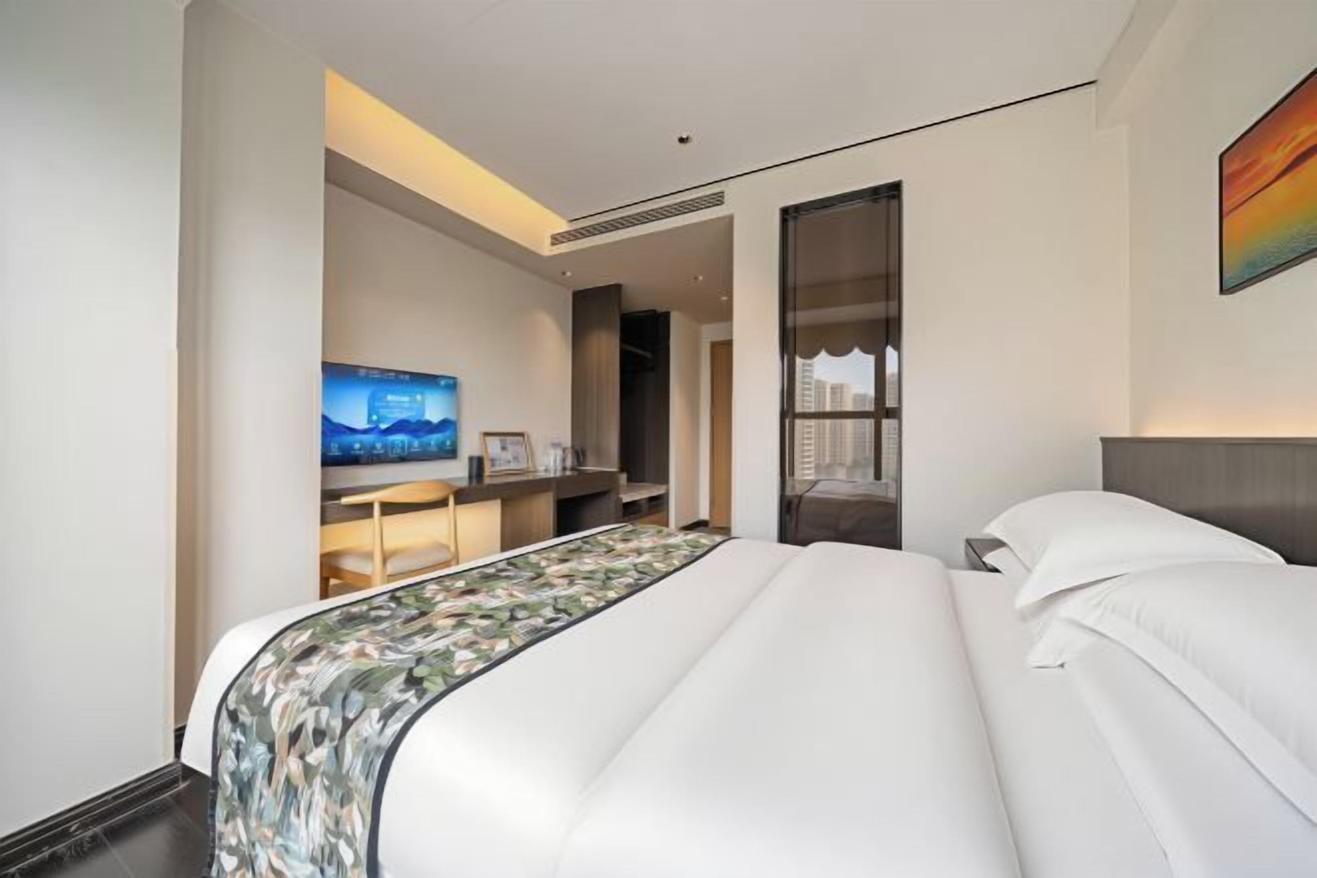 A hotel room with a large bed, a television, a desk, and a wardrobe.