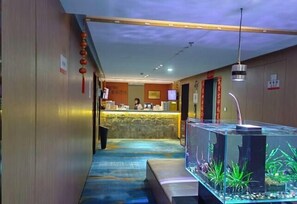 Um hall de hotel com uma mesa de recepção, um aquário e uma parede de pedra.