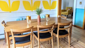 Un comedor con una mesa y sillas de madera, una planta en maceta y una pared con un diseño de hojas amarillas.