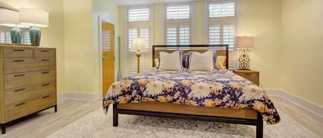 Quarto com cama, penteadeira, mesa de cabeceira, abajur e ventoinha no teto.