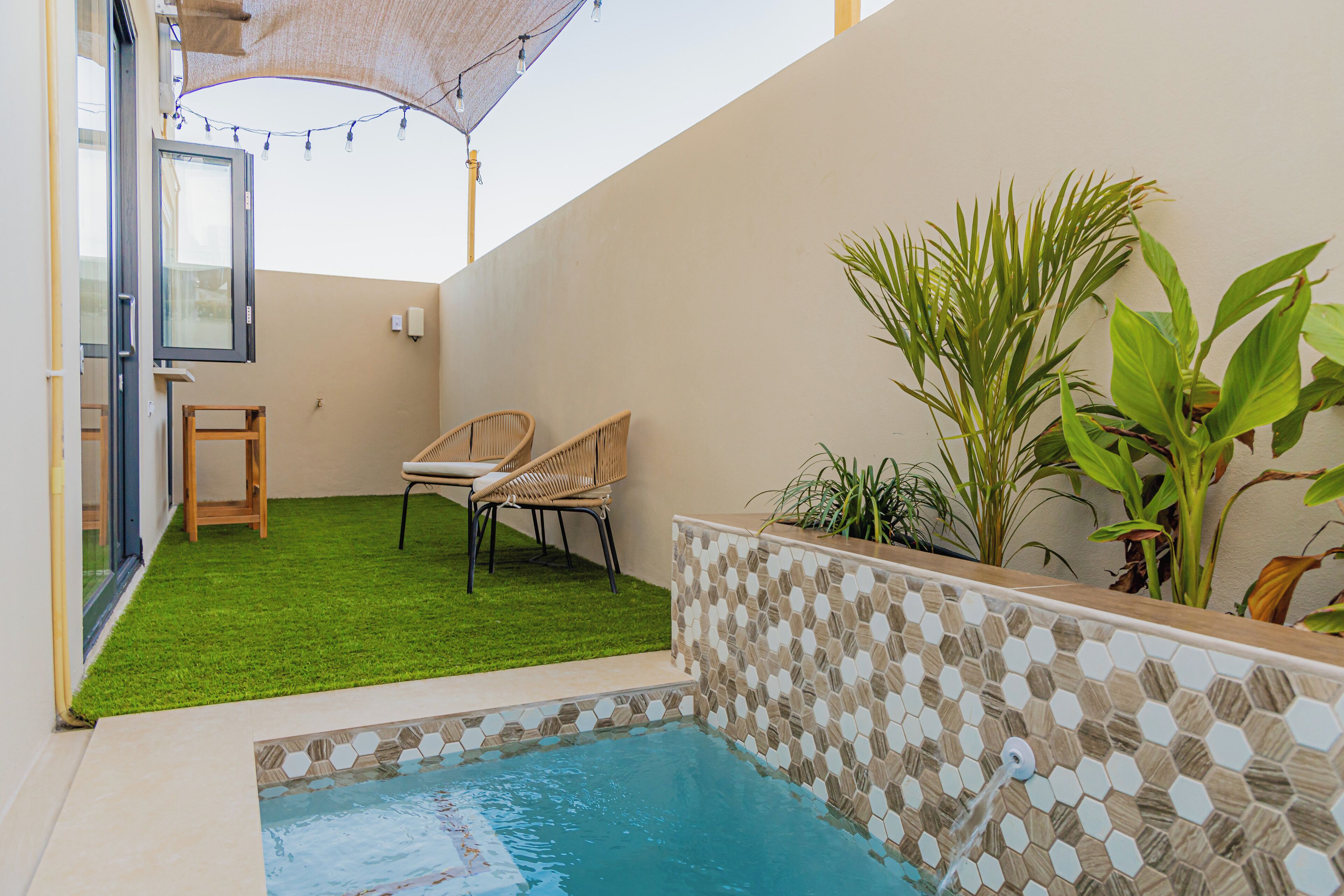A small outdoor pool area with a tiled edge, two wicker chairs, and a potted plant.