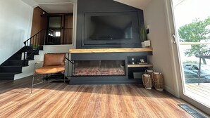 A modern living room with a fireplace, a large TV mounted on the wall, a staircase, and a view of the outdoors. - Swim, Sip, and Stay Awhile at this Beautiful Keuka Lake Retreat! (Dundee)