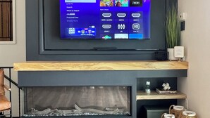 A modern living room with a flat-screen TV mounted on a dark wall above a wooden mantel. - Swim, Sip, and Stay Awhile at this Beautiful Keuka Lake Retreat! (Dundee)