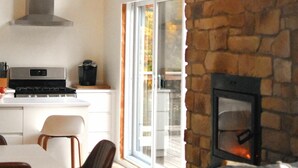 A modern kitchen with a stone wall, a fireplace, and a dining area with chairs and a table.