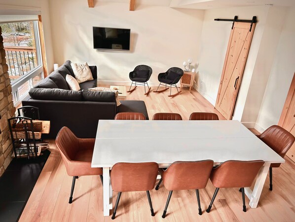 A modern living room with a sofa, a TV mounted on the wall, a dining table with chairs, and a sliding door closet.