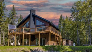 A modern log cabin with a wooden deck, large windows, and a solar panel.