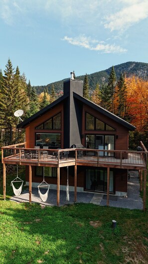 A modern house with a large deck, large windows, and a chimney.