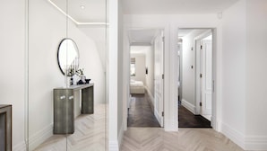 A hallway with a mirrored wardrobe, a bed, and a door leading to another room.
