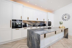 A modern kitchen with white cabinetry, a marble island, and a wall clock. - 1 Min Walk to Harrods | Knightsbridge Duplex (London)