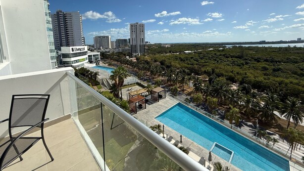 A balcony with a view of a swimming pool, palm trees, and high-rise buildings in the background. -  Phenomenal ocean view  2bed, 2 bath Apartment. (Cancún)