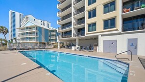 A swimming pool area with lounge chairs and a building with multiple balconies. - Island Winds West 471 (Gulf Shores)