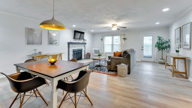 A modern living room with a fireplace, a dining area with a wooden table and chairs, and a ceiling fan. - 4 Bedroom Beachside Retreat – High - Speed WiFi Included (Virginia Beach)