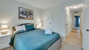 A bedroom with a bed, nightstands, a painting, and a hallway leading to another room. - 4 Bedroom Beachside Retreat – High - Speed WiFi Included (Virginia Beach)