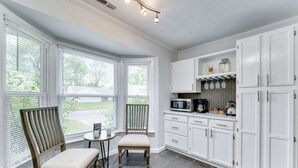 A kitchen with white cabinets, a microwave, and a coffee maker on the countertop. There are two chairs and a small table. - 4 Bedroom Beachside Retreat – High - Speed WiFi Included (Virginia Beach)