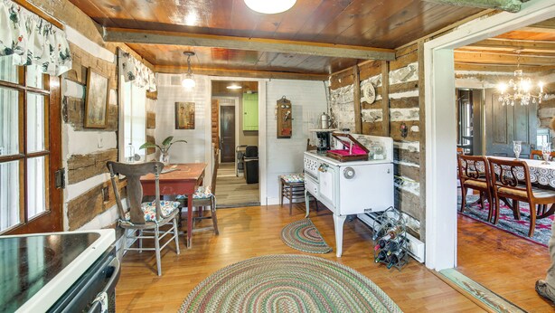 Una cocina rústica con vigas de madera, una estufa antigua y un comedor con sillas y mesa de madera.