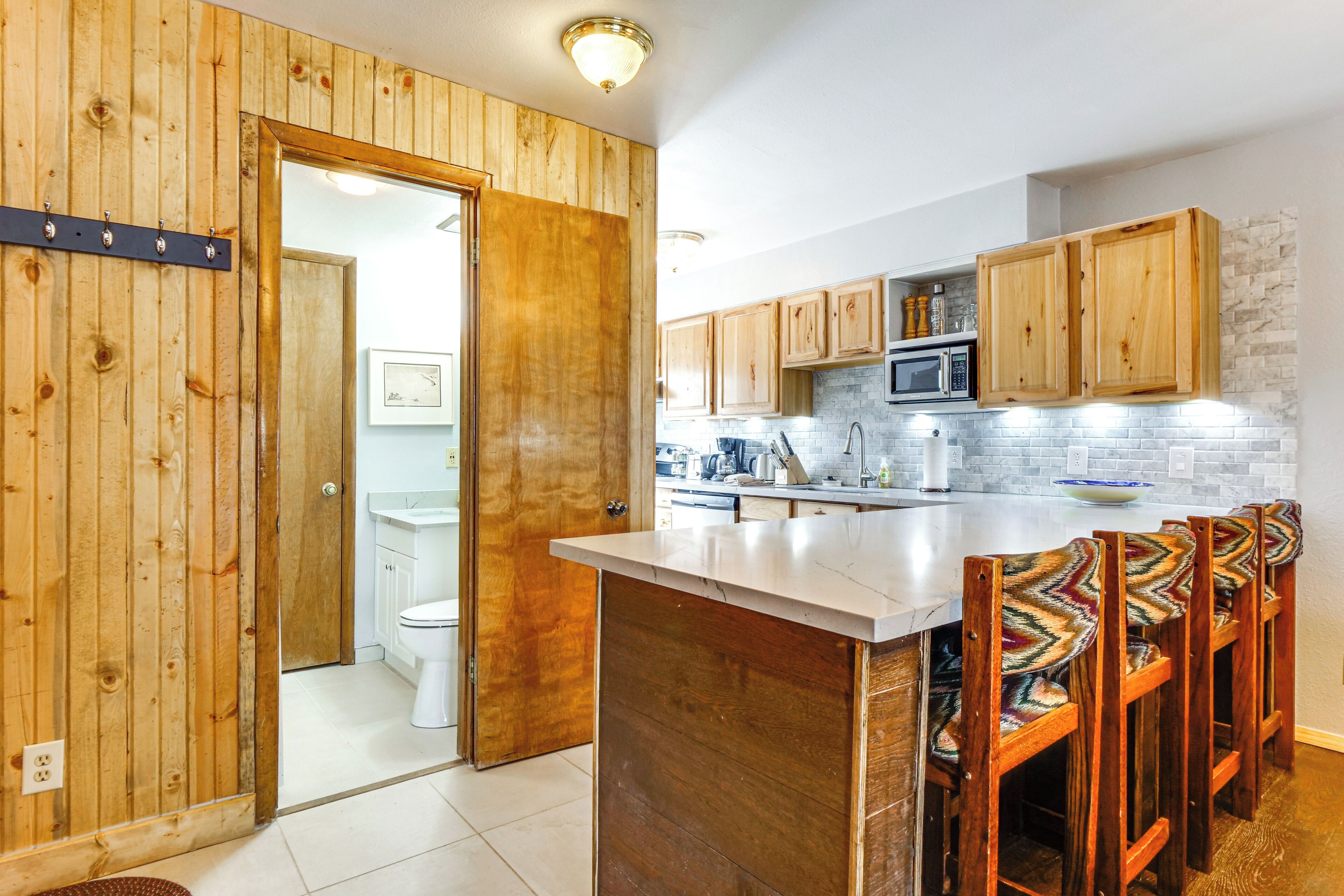 A kitchen with wooden cabinets, a white countertop, and a bar area with chairs.