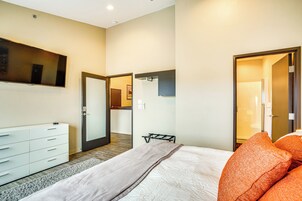 Un dormitorio moderno con una cama, un aparador, un espejo y una puerta que da a otra habitación.