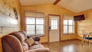 Een knus vakantiehuisje met houten inrichting, een bank, een eettafel met stoelen en een aan de muur bevestigde televisie.