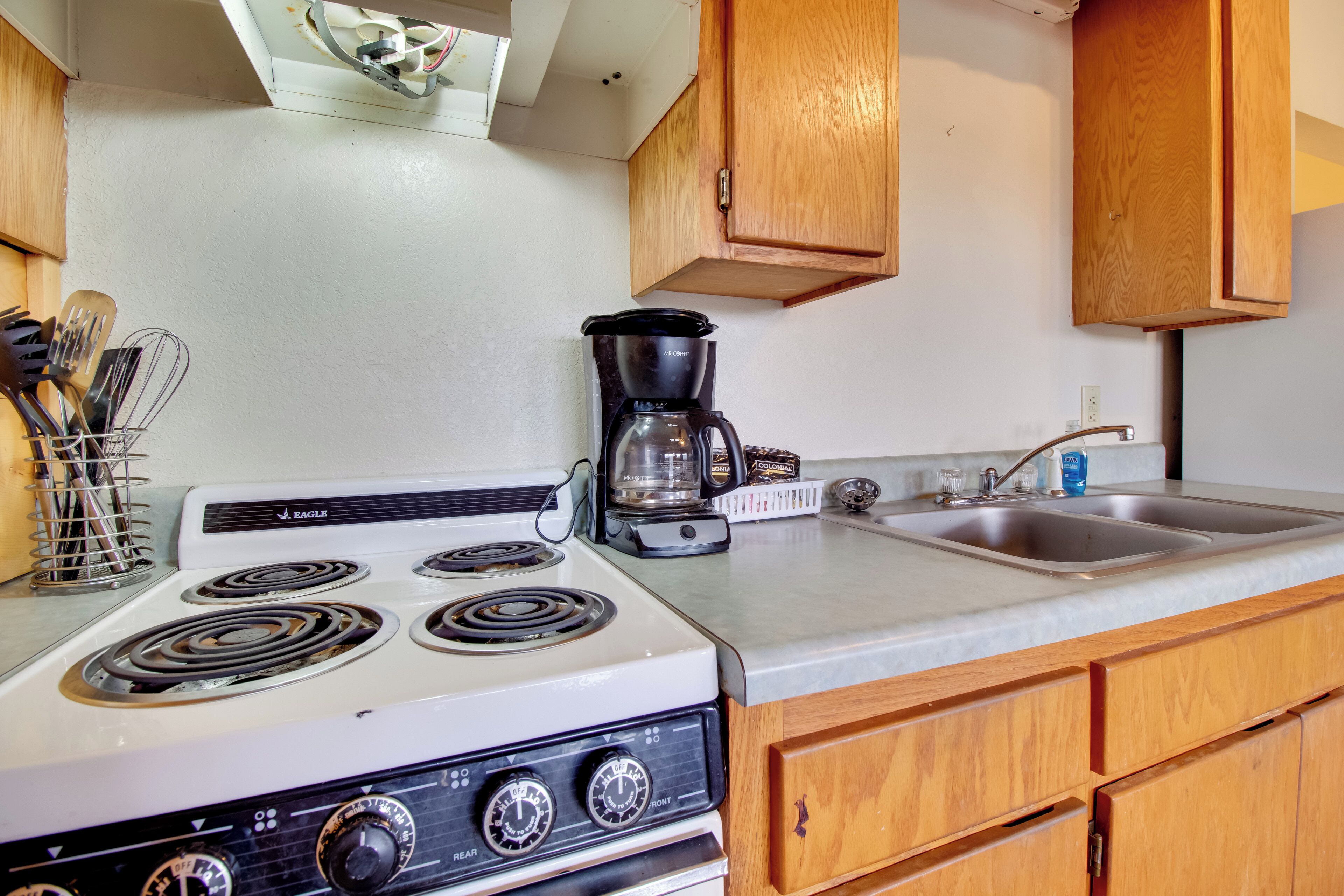 A kitchen with a white stove, wooden cabinets, a coffee maker, and a sink.