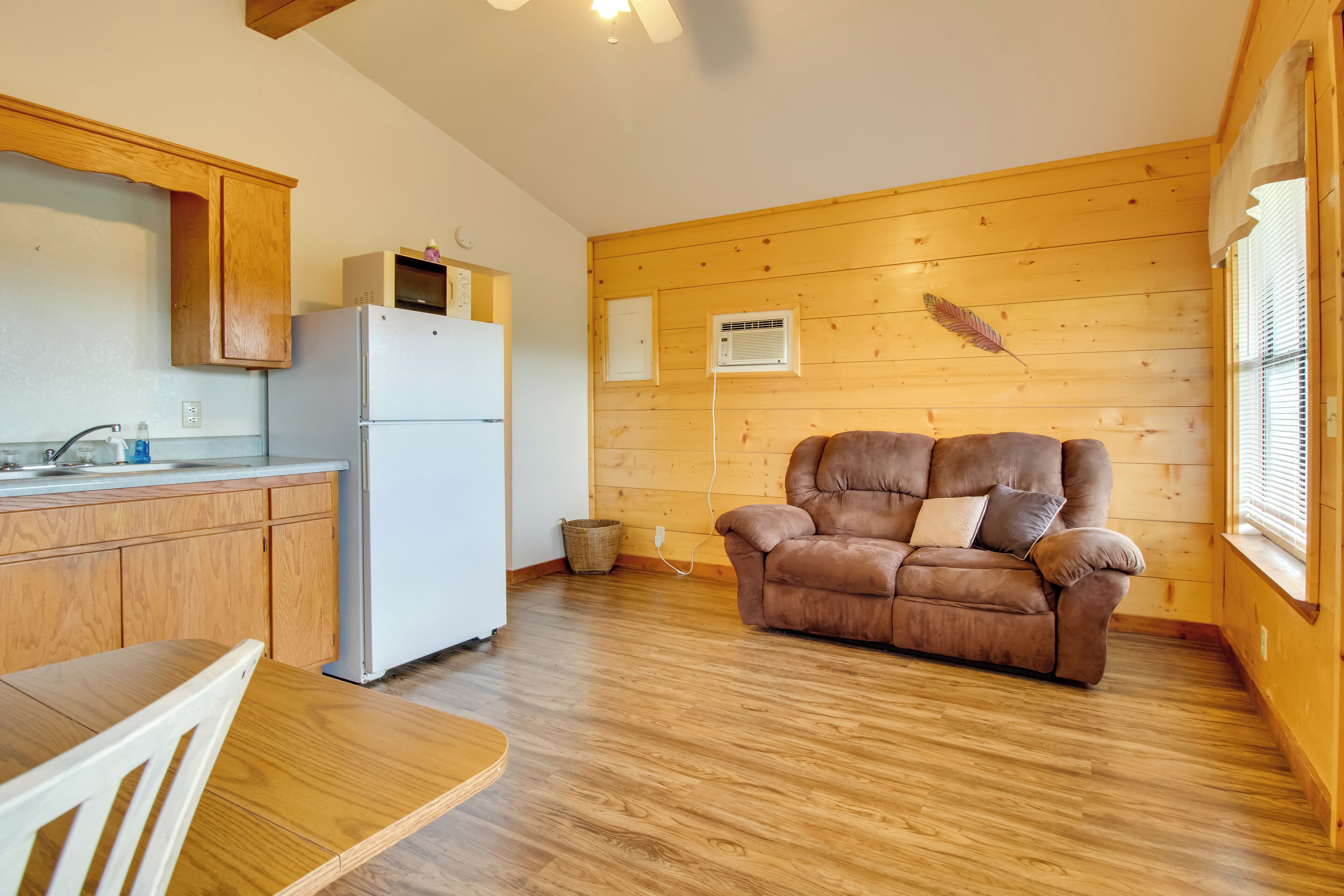 A cozy room with wooden walls, a brown leather sofa, a white refrigerator, and a wooden dining table.