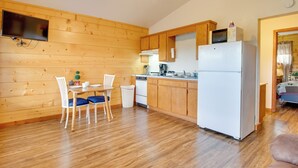 Een compacte keuken met houten kastjes, een witte koelkast, een magnetron en een eettafel met stoelen.