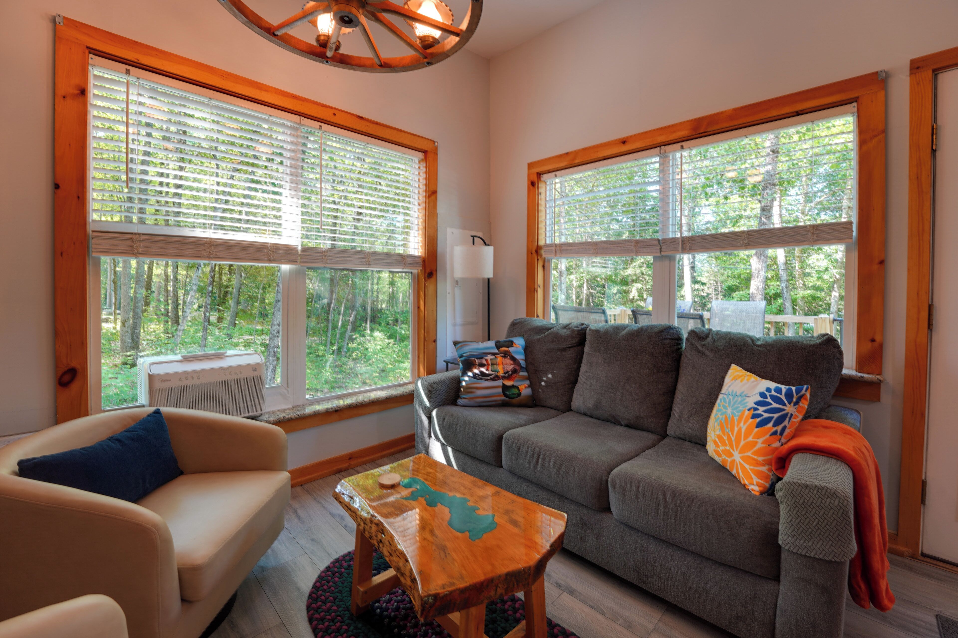A cozy living room with a sofa, a chair, a coffee table, and large windows with blinds.