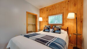 A bedroom with a wooden paneled wall, a window with blinds, a bed with a blue and white checkered blanket, two pillows with duck designs, and two floor lamps. - Private Dock & Deck: Tranquil Dam Pond Cottage! (Augusta)