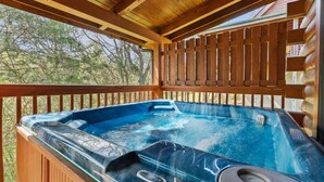 Een hottub met glazen omheining, houten terras en uitzicht op bomen.